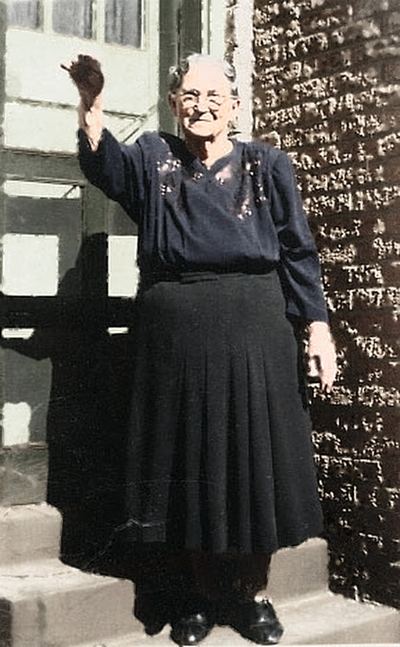 Restored and colorized (AI-assisted); faces are the original photo, colours are a best guess. Iona Belle Brock Bowles standing on a step, waving.