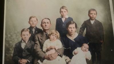 Restored and colorized (AI-assisted); faces are the original photo, colours are a best guess. J.D. and Lydia Mae Coffman with their children, studio group, c. 1915.