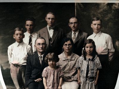 Restored and colorized (AI-assisted); faces are the original photo, colours are a best guess. J.D. and Lydia Mae Coffman family group, later years.