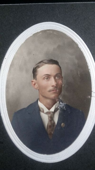 Restored and colorized (AI-assisted); faces are the original photo, colours are a best guess. James David 'J.D.' Coffman, oval portrait as a young man.
