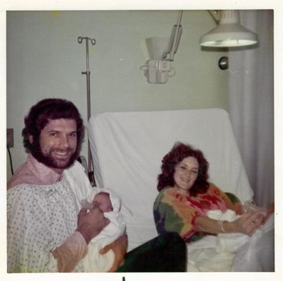 Nancy Proeger in hospital after a birth, with Bill holding the newborn, 1970s