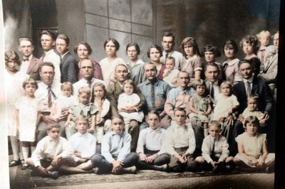 Restored and colorized (AI-assisted); faces are the original photo, colours are a best guess. Dee and Mollie Coffman family group photograph — fourteen people identified, Dee and Mollie among them.